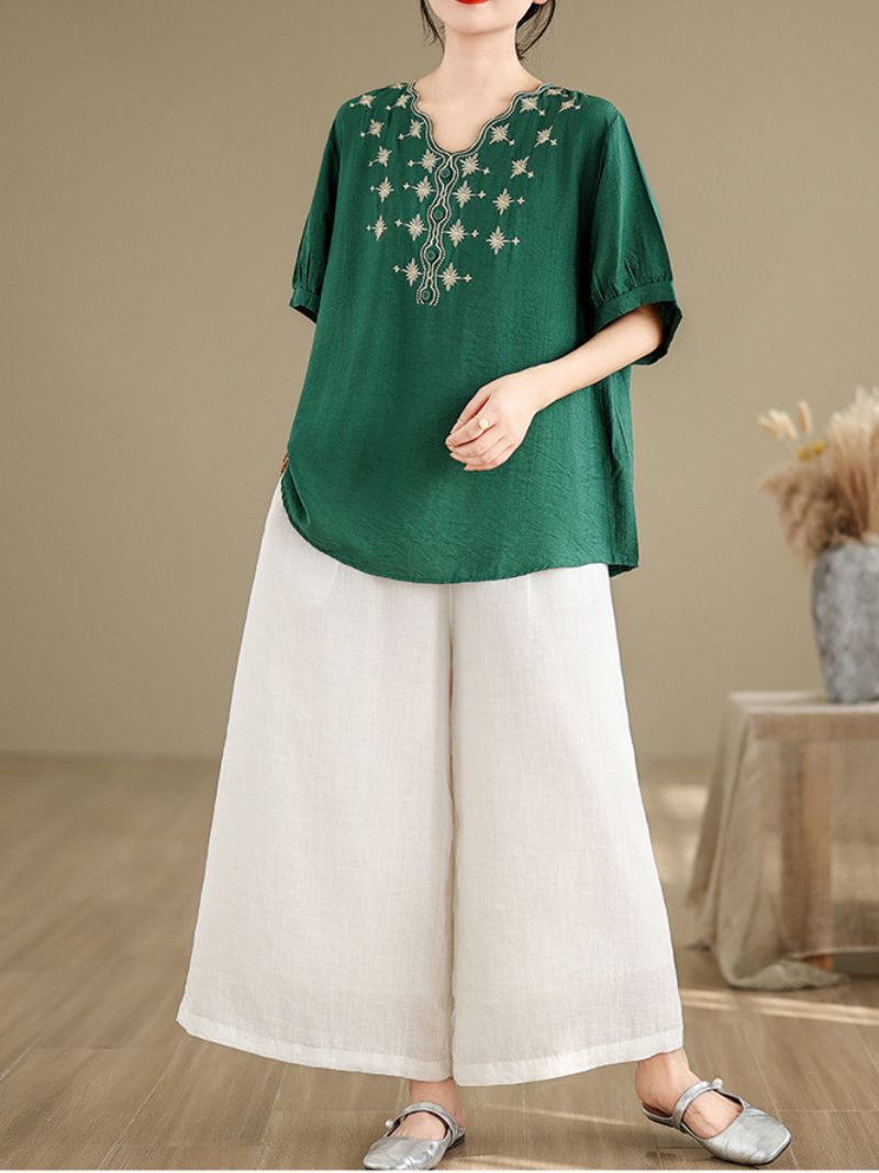 A woman wearing a green loose t-shirt top with embroidery around the neckline and three-quarter sleeves, paired with light beige pants.