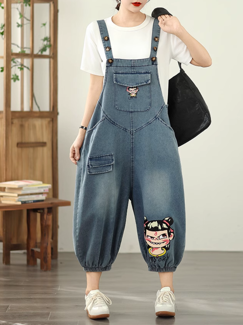 A woman wearing blue denim dungarees with a floral design on the leg, paired with a white t-shirt and sneakers.